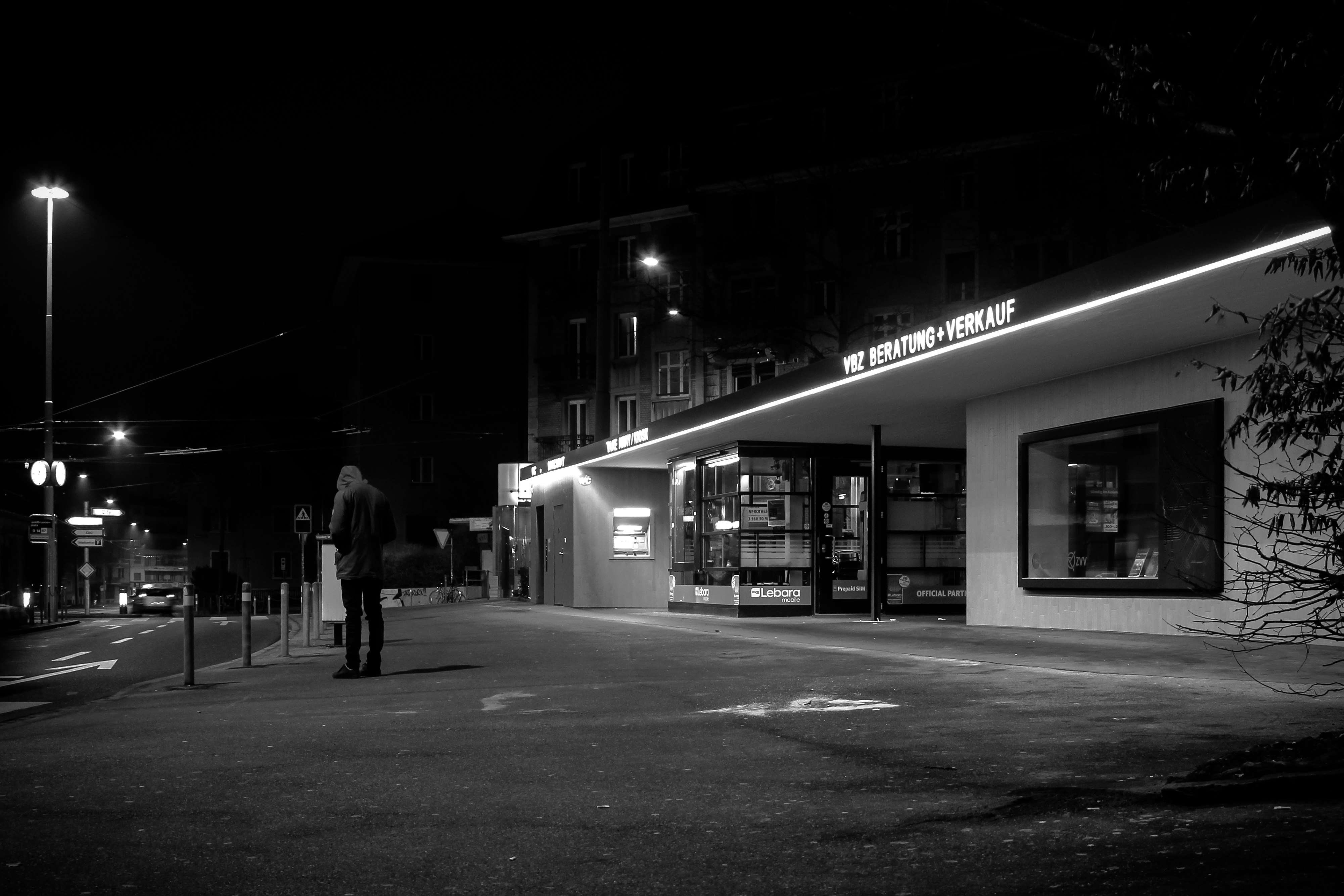 grayscale photo of man standing outside store